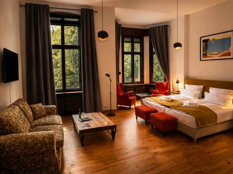 Suite im Schloss Reichenow mit Doppelbett, Sofa, hohen Fenstern und warmem Licht